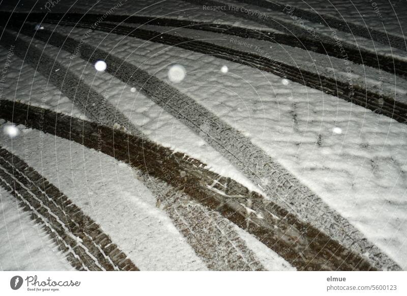 Autospuren auf einer schneebedeckten Straße mit angeblitzten Schneeflocken in der Nacht Spur grau in grau Schneedecke Reifenprofil Schmuddelwetter Winter