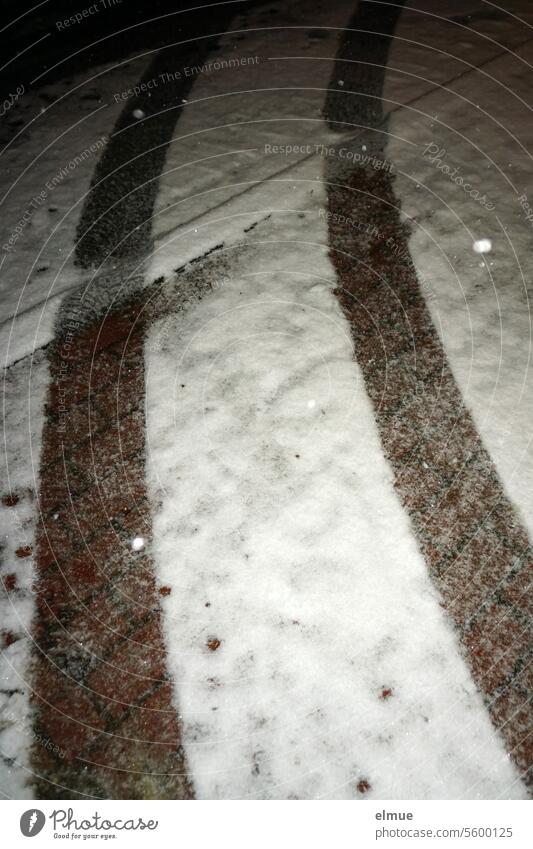 Autospur auf einem gepflasterten, verschneiten Weg mit angeblitzten Schneeflocken in der Nacht Schneespur Spur schneebedeckt Straßenpflaster Winter kalt