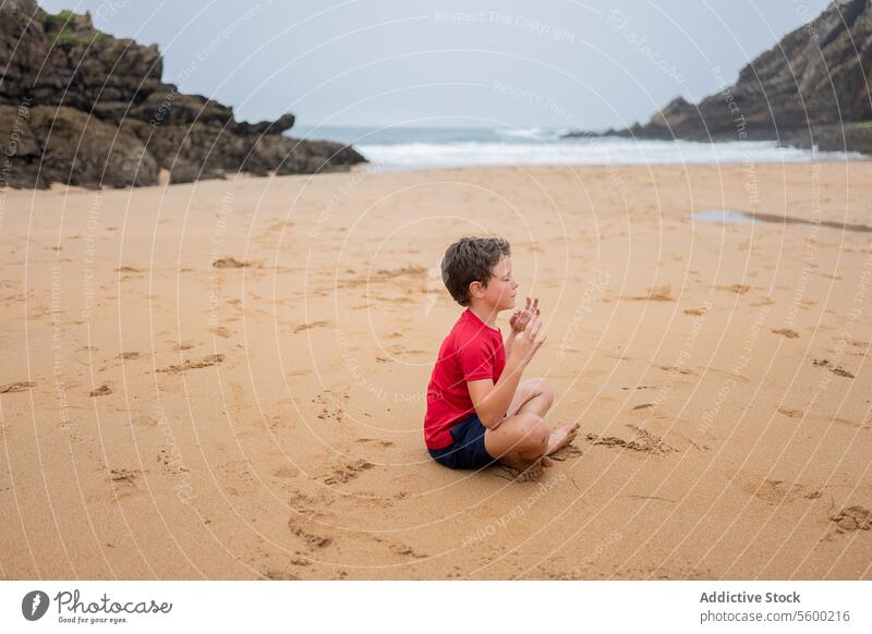 Nachdenklicher Junge an einem nebligen Strand Kontemplation Sand MEER bedeckt Klippe allein Sitzen Küstenstreifen Natur Einsamkeit im Freien reflektierend