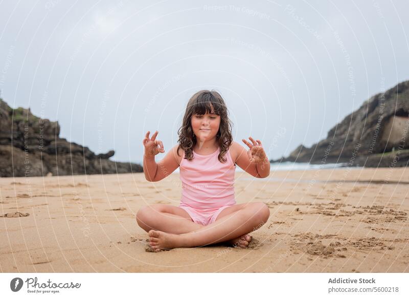 Junges Mädchen übt Yoga an einem Sandstrand Kinder Strand sandig Pose Windstille MEER Hintergrund jung heiter im Schneidersitz Sitzen praktizieren Wellness