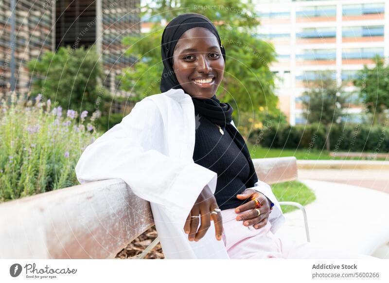 Glückliche Geschäftsfrau im Hidschab auf einer Bank in der Stadt sitzend Hijab Lächeln muslimisch formal Park Unternehmer Porträt selbstbewusst Großstadt Frau
