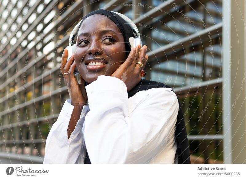 Glückliche Frau im Hidschab hört Musik in der Stadt Geschäftsfrau Hijab zuhören Kopfhörer Unternehmer professionell Beruf Manager Großstadt selbstbewusst