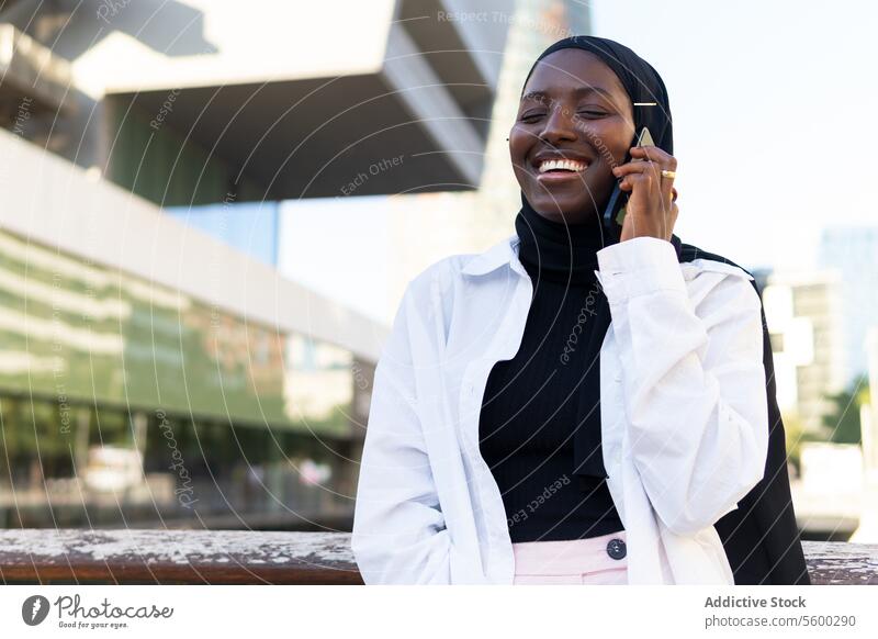 Glückliche Frau im Hidschab, die in der Stadt über ein Mobiltelefon spricht Geschäftsfrau Hijab reden Smartphone Augen geschlossen heiter Mobile Telefon modern