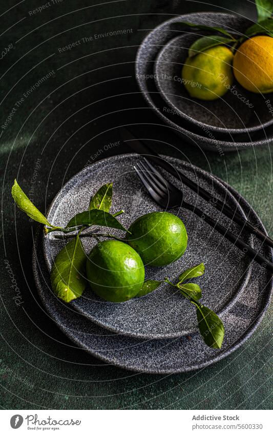 Frische Limetten auf dunklem Teller mit eleganter Präsentation Kalk grün Keramik Gabel dunkel Hintergrund weich Beleuchtung frisch Frucht Zitrusfrüchte Geschirr