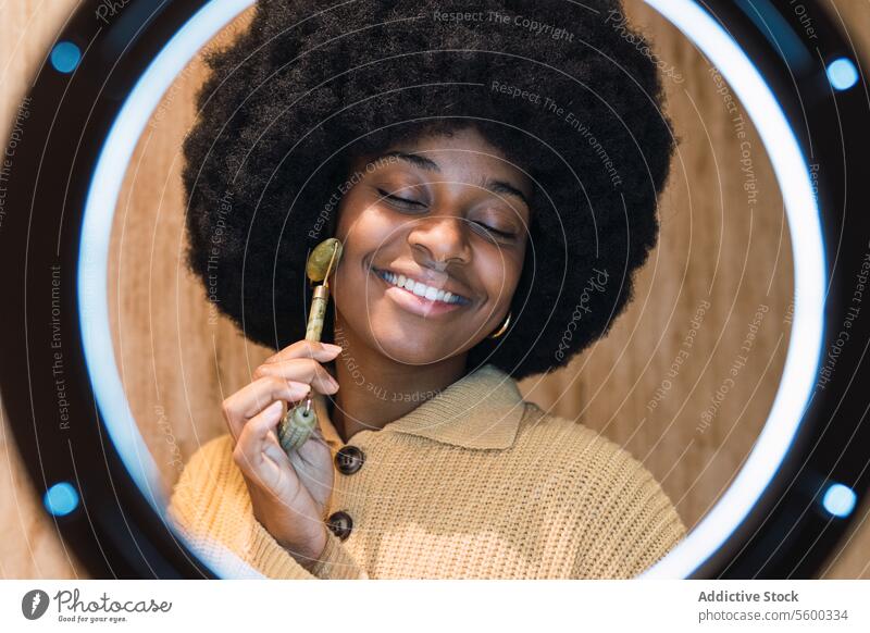 Schwarze Frau massiert ihr Gesicht mit einem Rollmassagegerät Massage Rolle Verfahren Schönheit Hautpflege Gesichtsbehandlung Routine Augen geschlossen