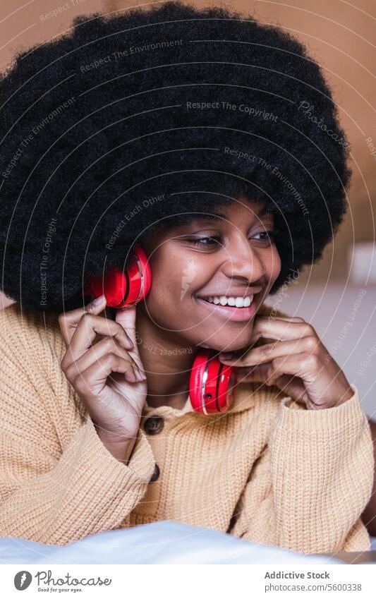 Lächelnde schwarze Frau, die mit Kopfhörern Musik hört zuhören benutzend Bett ruhen heimwärts Wochenende Kälte Afroamerikaner Afro-Look Apparatur