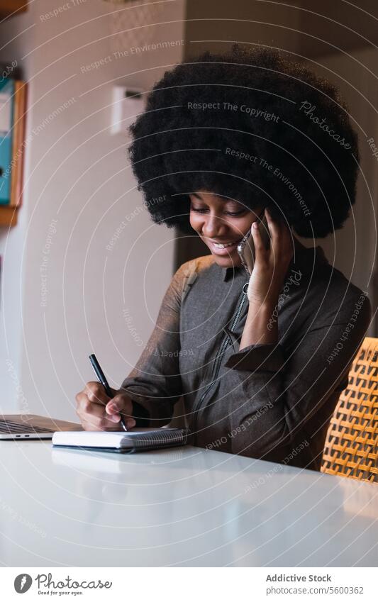 Positive schwarze Frau, die in ein Notizbuch schreibt, während sie telefoniert Smartphone Telefonanruf Gespräch diskutieren zur Kenntnis nehmen Notebook Arbeit