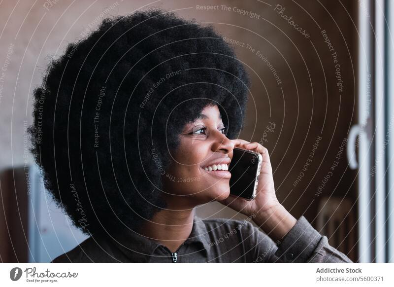 Fröhliche schwarze Frau, die mit einem Mobiltelefon spricht Smartphone Telefonanruf Afro-Look Lächeln Freizeit Frisur feminin Mobile Vorschein Glück Gespräch