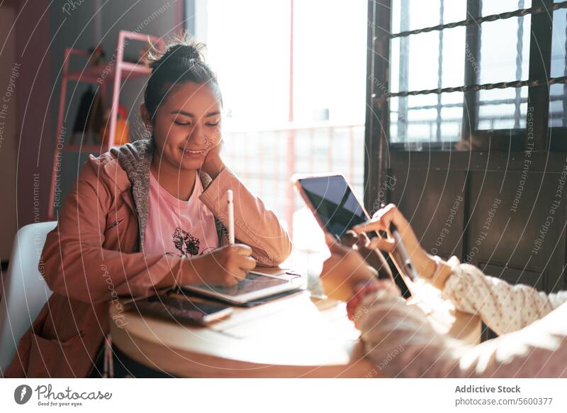 Eine junge Frau zeichnet einen Entwurf auf ihrem digitalen Tablet, während sie sich in einem Café um ihre Schwester kümmert junger Erwachsener Latein hispanisch