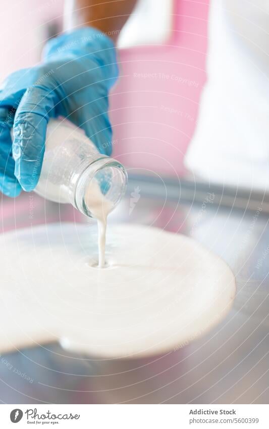 Ein Arbeiter schüttet Milch mit einem Glas auf eine rollende Eismaschine melken Sahne gerollt Speiseeis Tropfen liquide Tablett Abfertigungsschalter Belag weiß