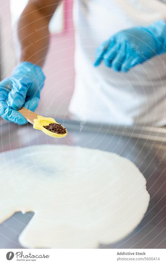 Ein Arbeiter bereitet in der Gefriermaschine ein gerolltes Eis mit Milch und Schokoladenstückchen zu. melken Sahne Chips Glas Löffel mischen Speiseeis Tropfen