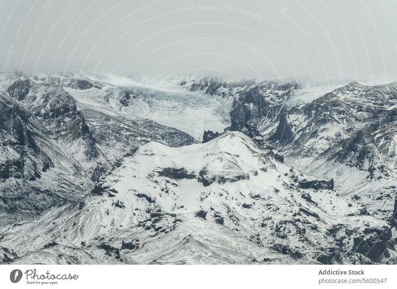 Luftaufnahme von Snowy Mountain Expanse unter grauem Himmel verschneite robust Landschaft Berge u. Gebirge Grate trist Natur Winter kalt im Freien Wildnis weiß
