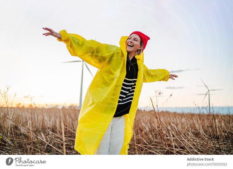 Energetische Person, die einen Sonnenuntergang in der Nähe von Windmühlen genießt Freude Fröhlichkeit Freiheit Feld gelb Regenmantel energetisch im Freien Natur