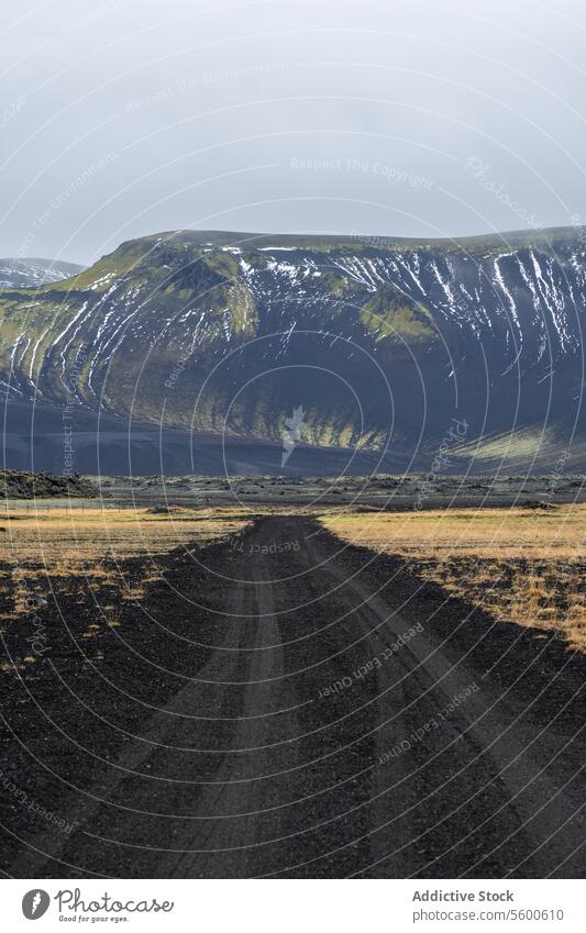 Abgelegene Schotterstraße, die zu einem verschneiten Berg in Island führt Hochland Berge u. Gebirge Schnee Landschaft abgelegen Einsamkeit Weite Gelassenheit