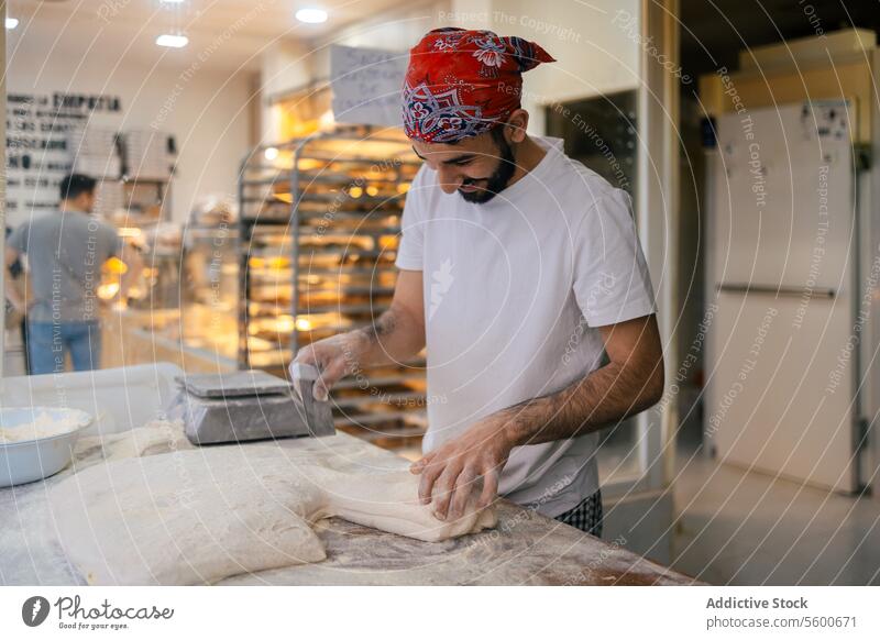 Arabischer Bäcker schneidet Teig mit dem Schulterblatt arabisch Teigwaren Brot Skala Gewichtung Vorbereitung Bäckerei Herstellung Glück Lächeln Mehl roh Tisch