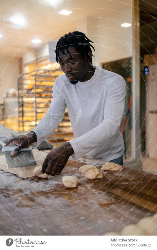 Schwarzer Bäcker schneidet Teig mit dem Schulterblatt schwarz Afro-Look Teigwaren Brot Vorbereitung Bäckerei Herstellung Mehl roh Tisch frisch Kutter Utensil