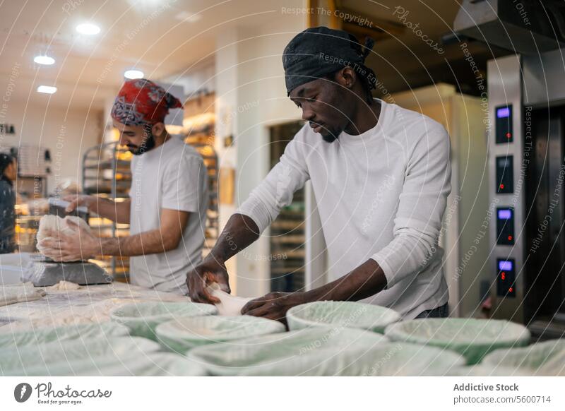 Schwarzer Bäcker beim Kneten in einer Bäckerei mit einem Kollegen schwarz Afro-Look Teamwork multiethnisch Teigwaren Kunstgewerbler Mehl Schimmelpilze Brot