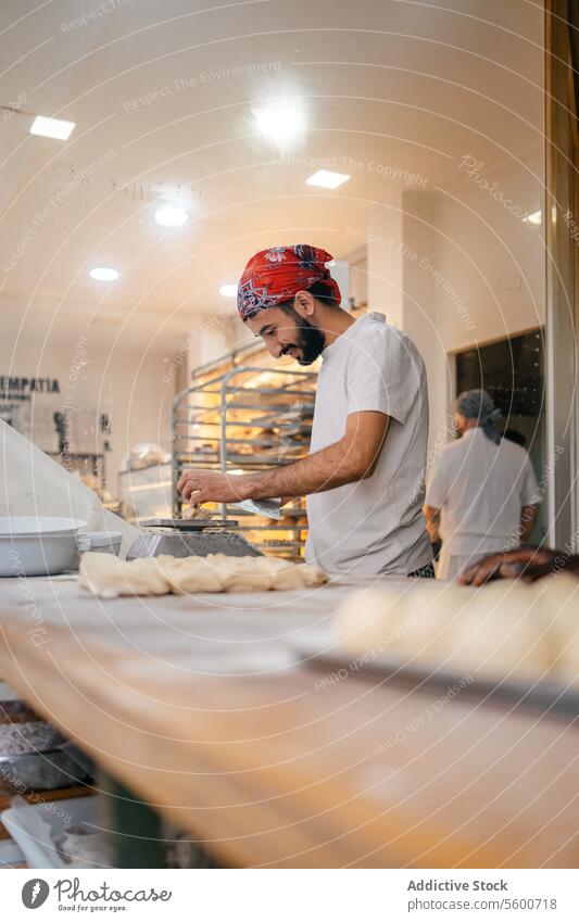 Arabischer Bäcker wiegt Teig mit Waage arabisch Teigwaren Schulterblatt Brot Skala Gewichtung Vorbereitung Bäckerei Herstellung Glück Lächeln Mehl roh Tisch