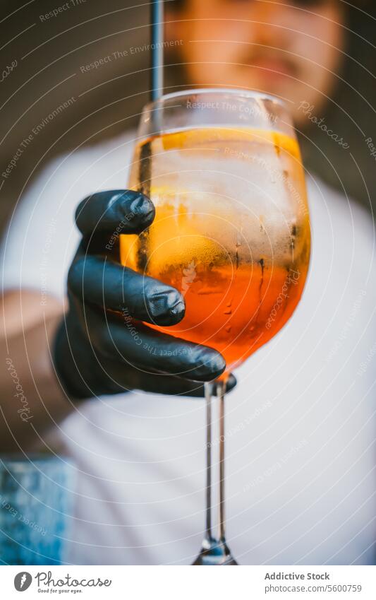 Anonymer Barkeeper mit Handschuhen, der einen Orangencocktail mit Eis und Strohhalm hält Barmann Cocktail orange Getränk Alkohol Weinglas Dienst Mixologie