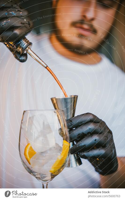 Konzentrierte junge professionelle Barkeeperin gießt Orangengetränk in Jigger, während sie einen erfrischenden Cocktail zubereitet und an der Theke in der Bar steht