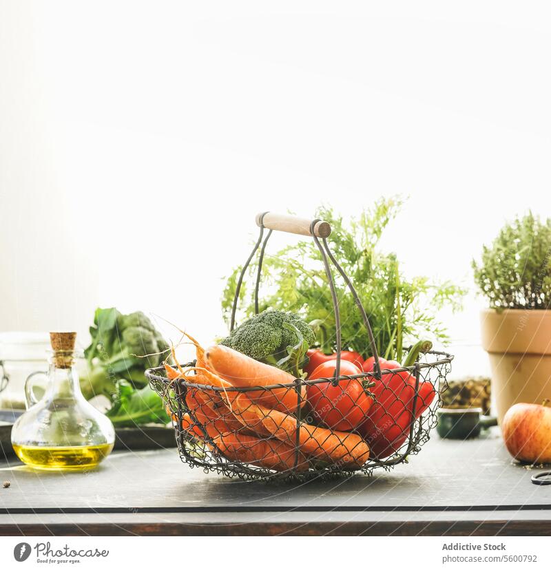 Metall-Lebensmittelkorb mit Bio-Gemüse: Karotten, Brokkoli, Paprika und Tomaten auf dem Tisch mit anderen gesunden Zutaten am Fenster Hintergrund mit Sonnenlicht. Gesunder Lebensstil. Vorderansicht.