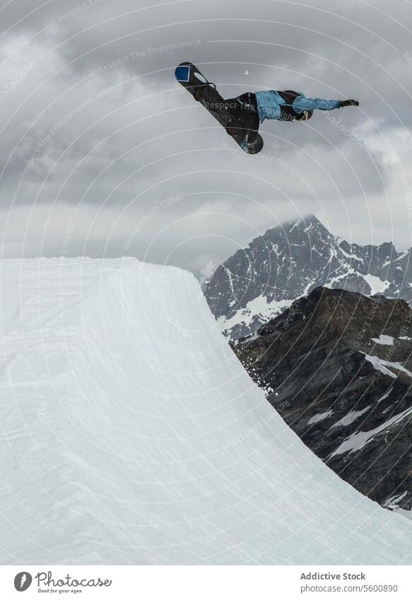 Seitenansicht eines anonymen Mannes mit Snowboard, der auf einem verschneiten Berg gegen einen bewölkten Himmel springt, während eines Urlaubs in den Schweizer Alpen