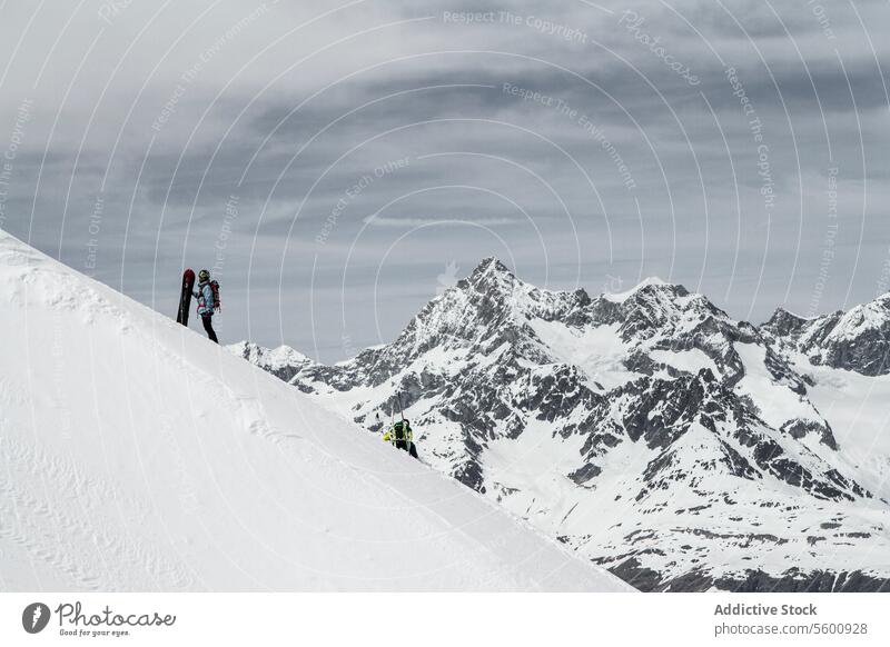 Seitenansicht eines anonymen Bergsteigers mit Snowboard auf einem schneebedeckten Hang gegen einen bewölkten Himmel im Winterurlaub in den Schweizer Alpen