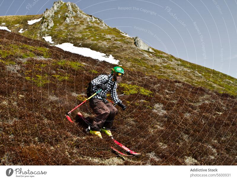 Seitenansicht eines jungen Mannes in Freizeitkleidung beim Skifahren auf einer Wiese im Urlaub in den Schweizer Alpen Wanderer Gras Hügel Ganzkörper sorgenfrei