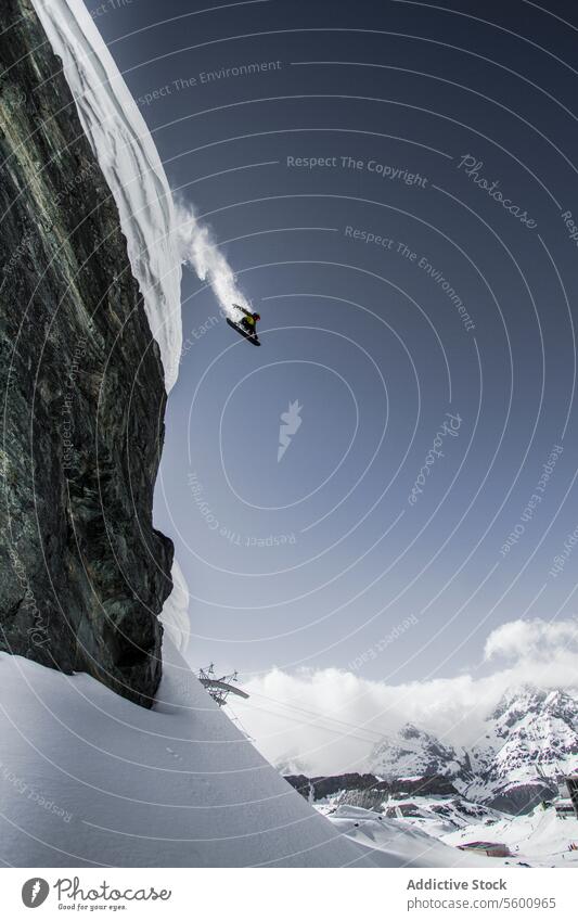 Seitenansicht eines anonymen Snowboarders, der im Urlaub von einem Berg gegen einen klaren Himmel in den Schweizer Alpen springt springen Berge u. Gebirge