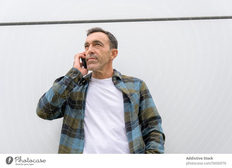 Nachdenklicher Mann, der mit seinem Smartphone spricht männlich Apparatur Gerät reden Mobile lässig Gespräch Telefon Stil benutzend modern kariertes Hemd