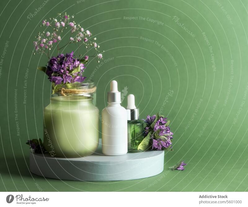 Natürliche kosmetische Produkt Einstellung mit Pipette Flasche, Kerze und Blumen auf Podium auf grünem Hintergrund. Gesundes Hautpflegekonzept mit natürlichen Produkten für die Gesichtsbehandlung. Vorderansicht.