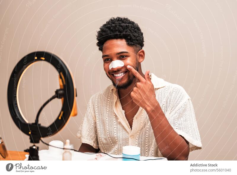 lateinamerikanischer Mann, der seine Haut mit einem Nasenstreifen und einem Lächeln pflegt Hautpflege Routine Nasenleiste Pflege Tisch Produkte Ringlicht