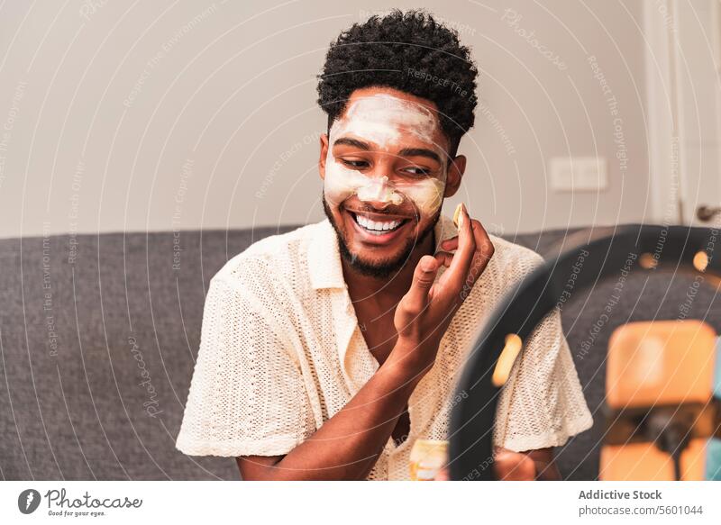Lateinamerikanischer Mann trägt Gesichtsmaske während Videoblog-Sitzung auf Hautpflege heimwärts Schönheit Pflege Streaming lässig Spiegel Ringlicht Liege