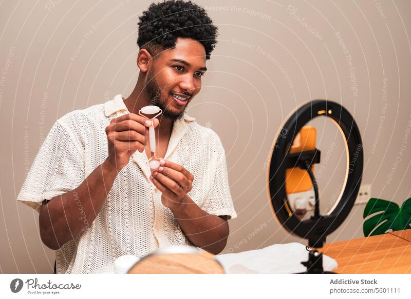 lateinamerikanischer Mann bei der täglichen Pflegeroutine mit Gesichtsroller Hautpflege Spiegel Lächeln Routine Selbstfürsorge jung Schönheit Gesundheit