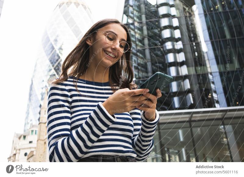 Lächelnde Frau mit Smartphone im Londoner Stadtbild Großstadt urban Skyline Glück gestreift Top Engagement Telefon Gebäude modern Technik & Technologie