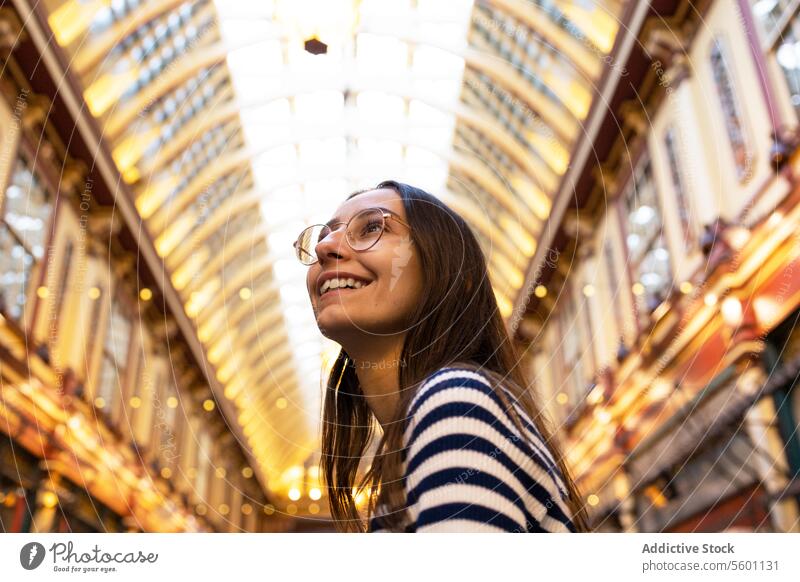 Lächelnde junge Frau beim Erkunden eines Londoner Marktes im Innenbereich Erkundung Architektur reisen Tourist heiter Bewunderung kultig bedeckt gestreift Hemd