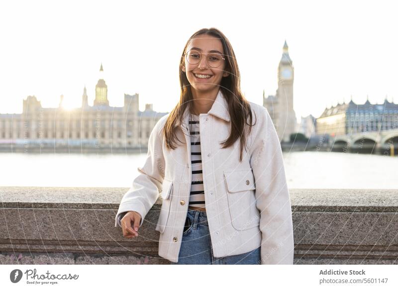 Lächelnde junge Frau genießt in London mit Big Ben im Hintergrund Parlament sonnig Tag Themse Mode Mantel Glück reisen Tourismus Wahrzeichen Briten England