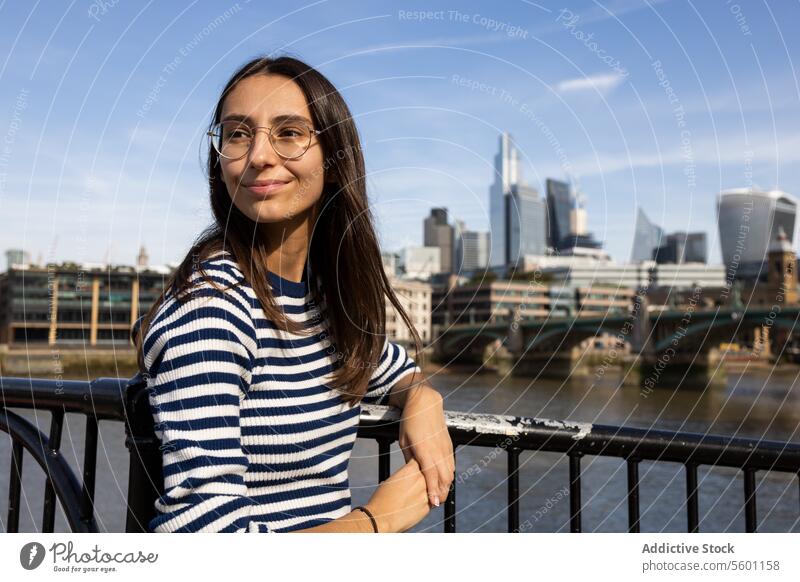 Junge Frau genießt das Stadtbild an der Themse London Brille Lächeln gestreift Hemd Fluss Hintergrund jung Erwachsener Freizeit reisen Tourismus im Freien
