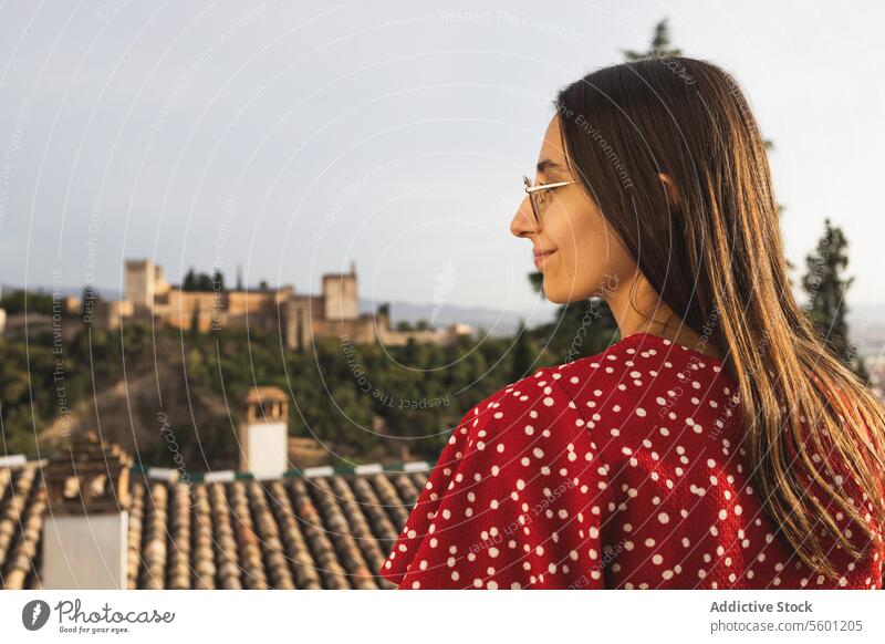 Seitenansicht eines glücklichen Touristen, der vor der historischen Alcazaba steht, während er seinen Urlaub in Granada, Spanien, genießt Frau Brille Lächeln