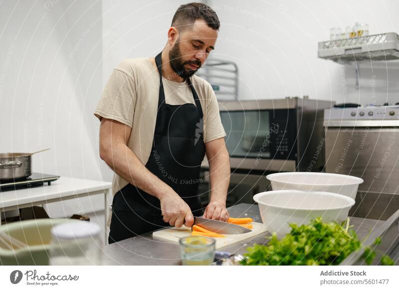 Junger Koch schneidet Karotten Küchenchef Essen zubereiten Lebensmittel professionell Restaurant Gemüse Messer Schneiden Mann jung Arbeit männlich Speise Person