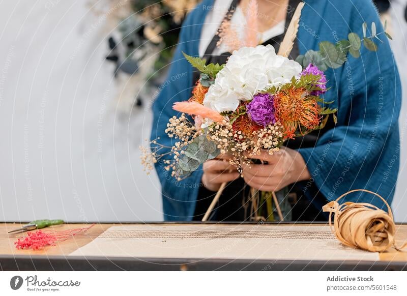 Anonyme Person beim Basteln eines Blumenstraußes mit Blumen Blumenhändler Ordnung Hortensie Blütezeit Werkstatt Tisch hölzern Schürze blau Zusammenbau Handwerk
