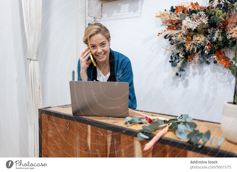 Florist, der eine telefonische Bestellung mit einem Laptop am Tresen entgegennimmt Frau Blumenhändler Handy Abfertigungsschalter Lächeln Business Arbeit