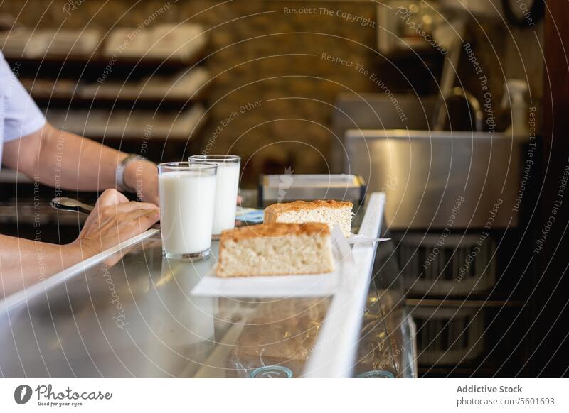 Unbekannte Person stellt zwei Gläser mit Milch und Kuchen auf den Tresen melken Glas Abfertigungsschalter Bäckerei Arme Lebensmittel Molkerei trinken Brot