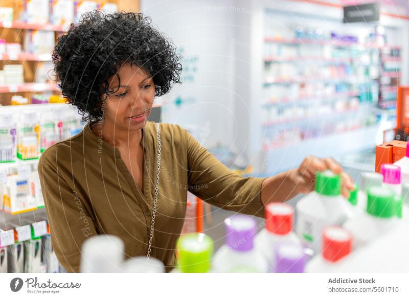 Kunde prüft Flaschen im Regal eines Apothekengeschäfts Frau Drogerie Afrohaar schön prüfen Bestandteil Medizin angeordnet Laden kaufen Käufer Medikament