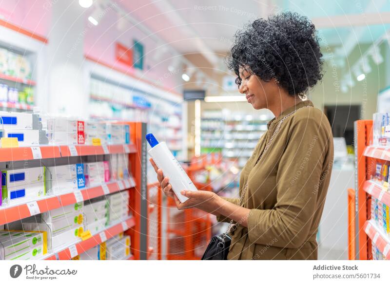 Schwarze Frau hält Flasche in einem Apothekenladen Hand prüfen Information vorgeschrieben Produkt kennzeichnen Drogerie verschwommener Hintergrund Nahaufnahme