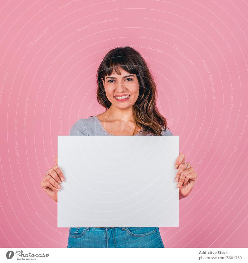 Lächelnde Frau hält ein leeres Schild vor einem rosa Hintergrund Erwachsener attraktiv schön Schönheit blanko braune Haare Geschäftsfrau Textfreiraum Ethnizität