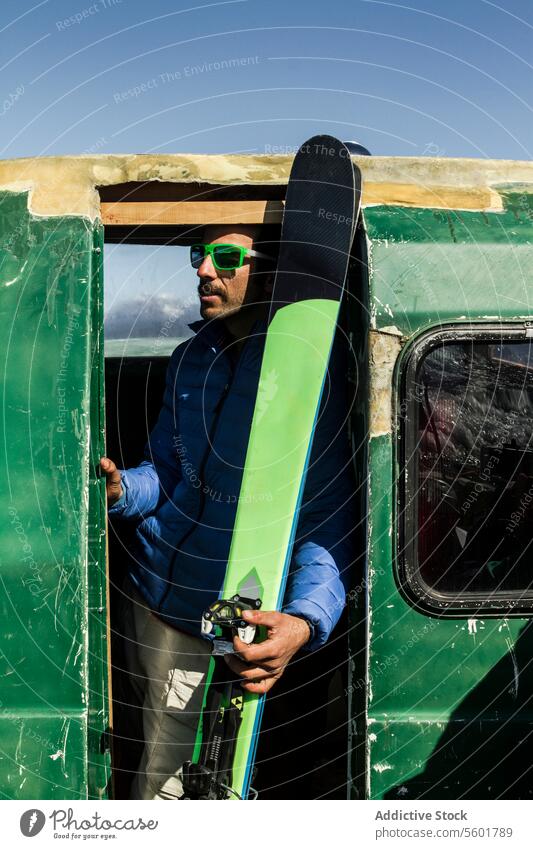 Mann mit Snowboard im Auto stehend Snowboarder warme Kleidung Sonnenbrille Eingang Fahrzeug grün Schweizer Alpen Urlaub Verkehr Sport Stehen Lifestyle genießen