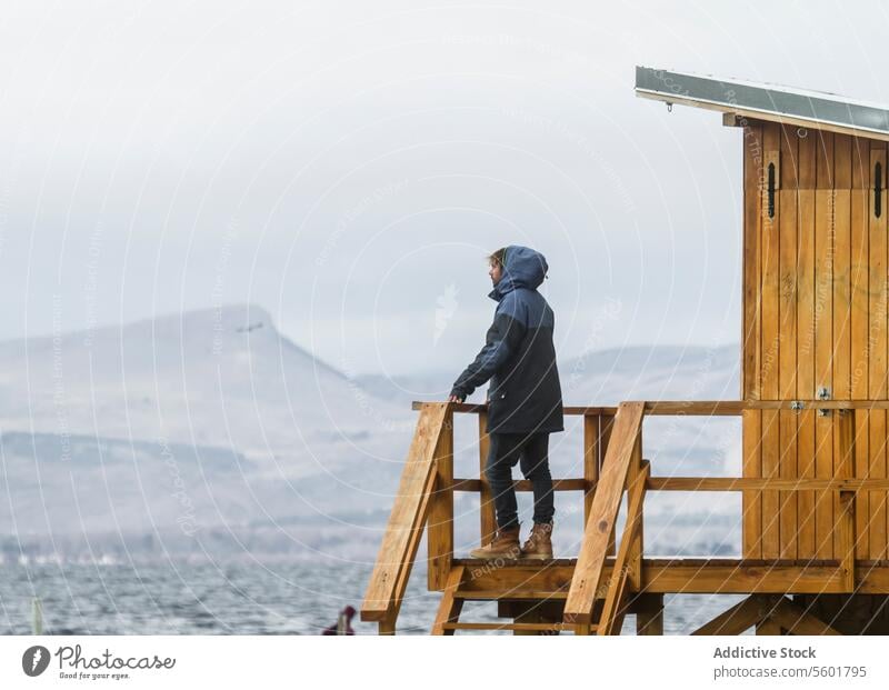 Mann steht am Aussichtspunkt und genießt den Winterurlaub unkenntlich Urlaub Seitenansicht mit Kapuze hölzern Turm Himmel verschwommener Hintergrund Ganzkörper