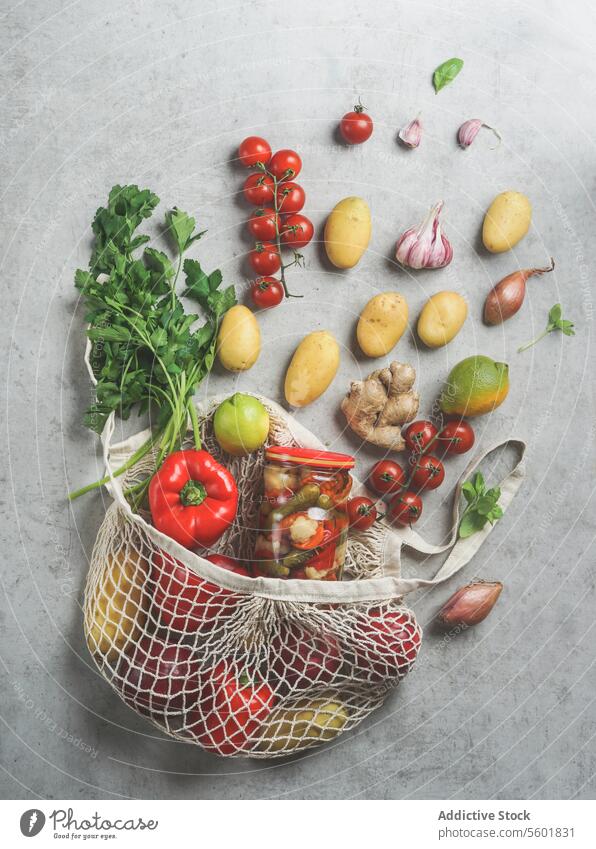 Nachhaltige Lebensmittel Einkaufstasche mit verschiedenen Gemüse: Kartoffeln, Tomaten, Paprika, Limette, Kräuter, Knoblauch, Zwiebel und Konserven auf grauem Beton Tisch. Plastikfreier Lebensstil. Ansicht von oben. Null Abfall