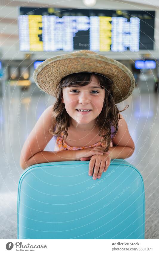Glückliches Mädchen mit Strohhut und blauem Koffer auf dem Flughafen beim Warten auf den Abflug im Flughafenterminal Porträt Urlaub Feiertag Gepäck Lächeln Hut